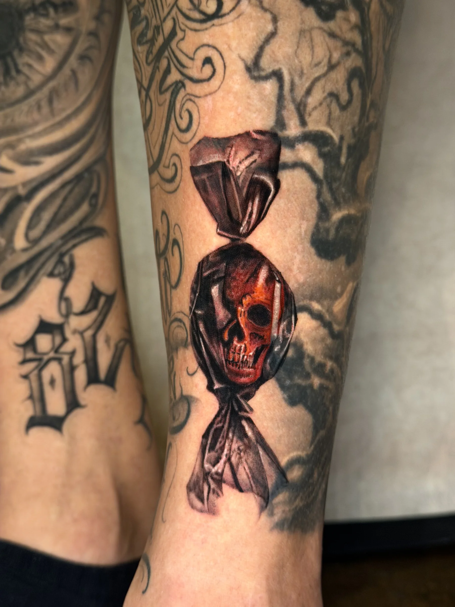 Skull inside a candy wrapper tattooed on a lower leg